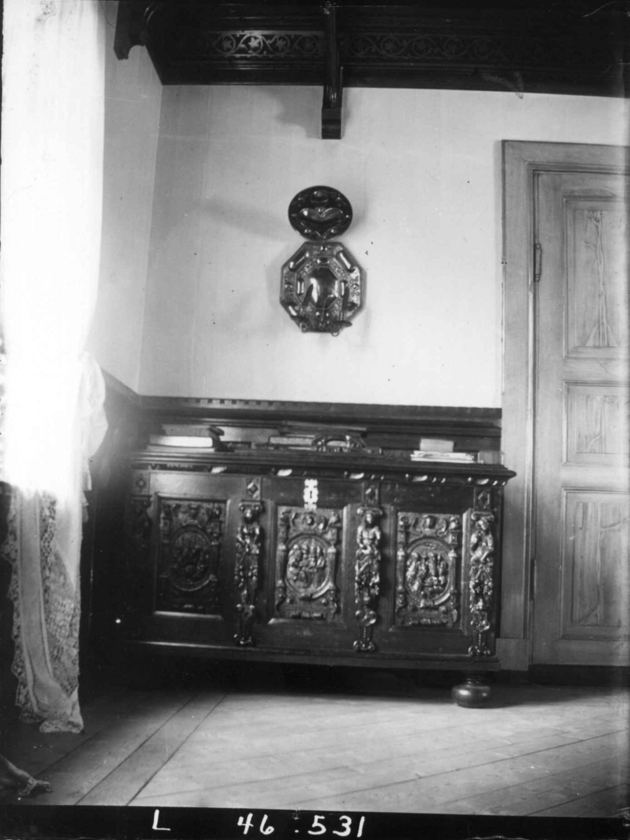Interiør, Dal gård, Ullensaker. Rom med utskåret kiste, lysskjold på veggen.
Fra serie fotografert av kammerherre Fredrik Emil Faye (1844-1903), gårdens eier.
