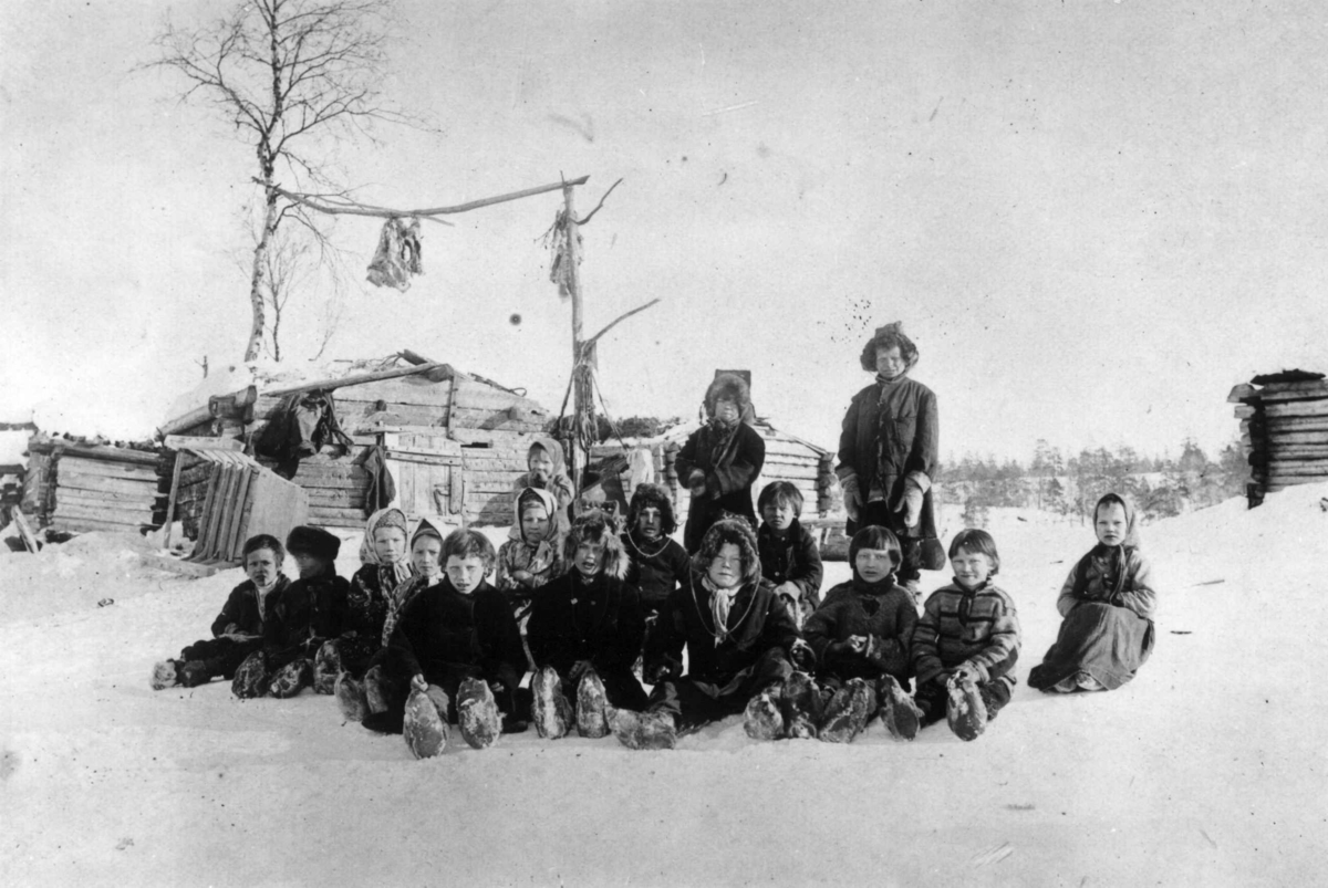 Skoltesamiske skolebarn sitter i snøen ved Pasvik-siidaens skole, Pasvik, Sør-Varanger, Finnmark, 1898.