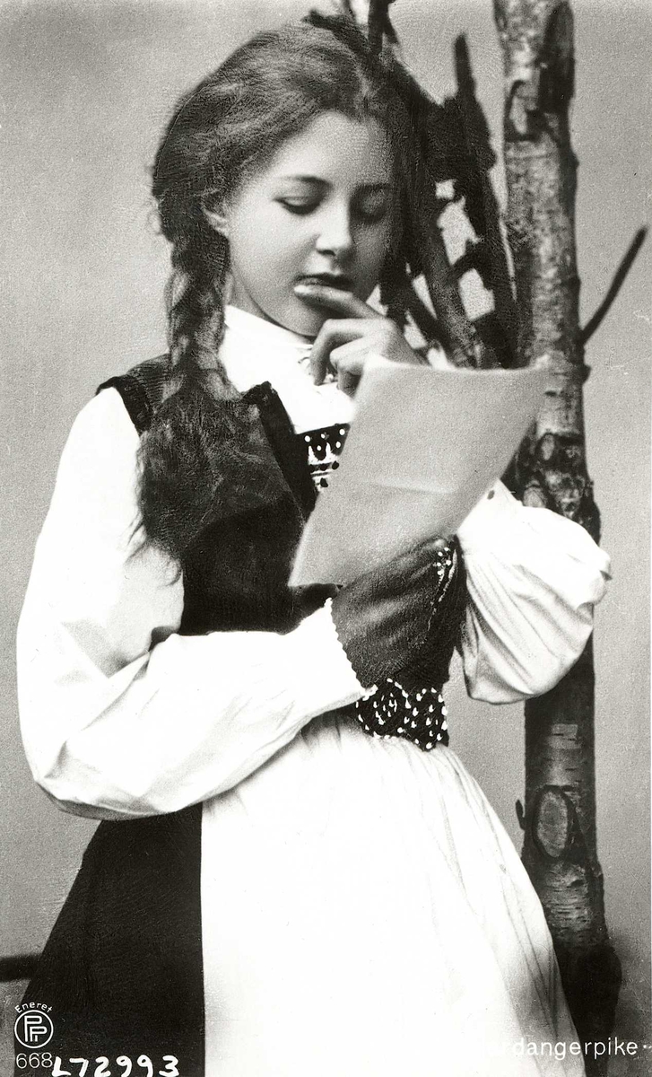 Studiofotografi av en ung kvinne som leser. Drakt fra Hardanger.