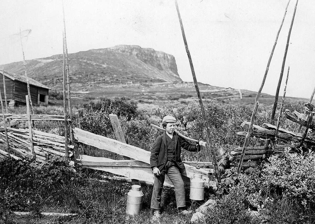 Gutt ved skigard med åk med 2 melkespann, antatt ved Skeikampen, Gausdal, Oppland.
Serie tatt av Robert Collett (1842-1913), amatørfotograf og professor i zoologi. 