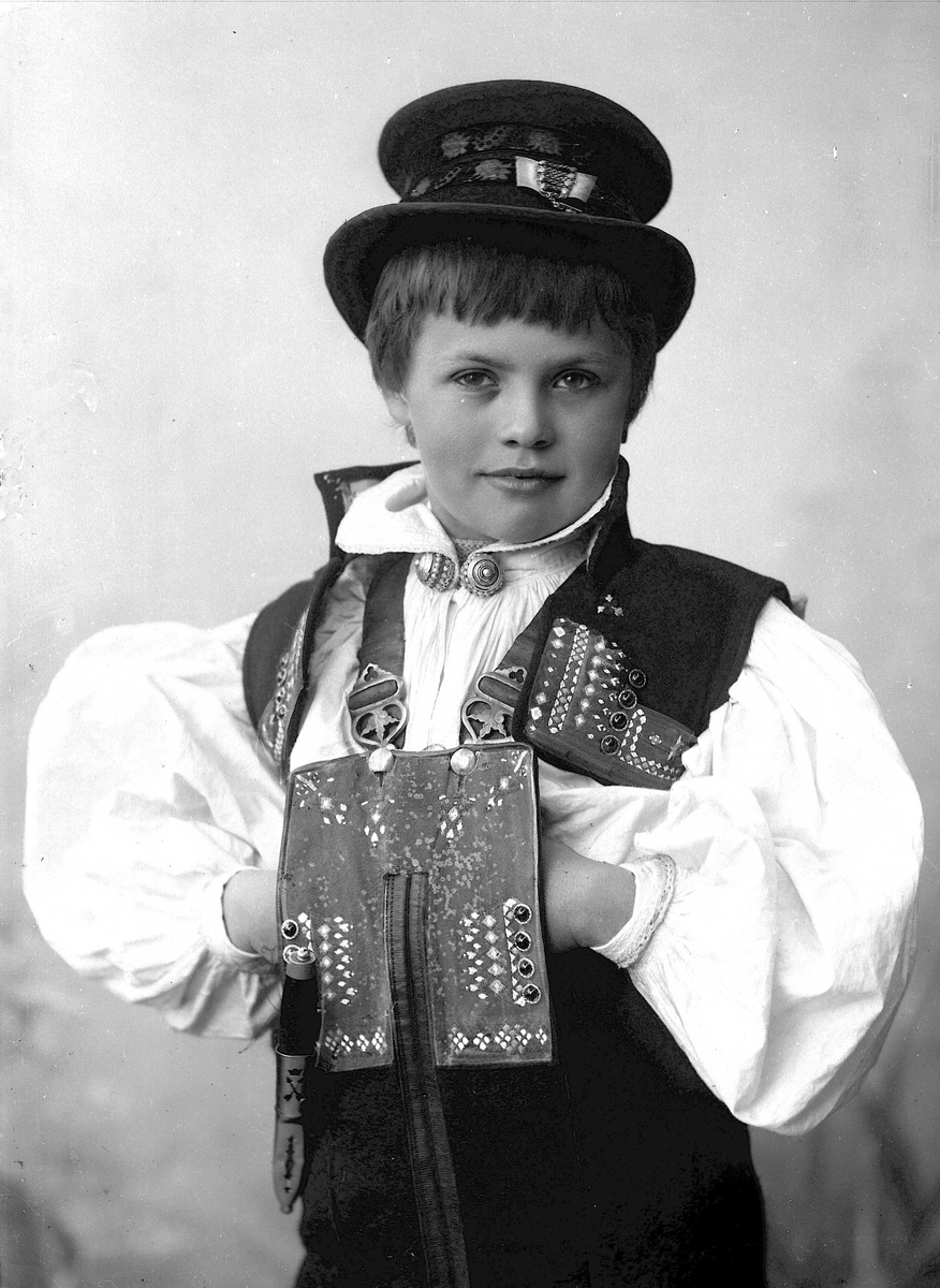 Studioportrett av ung gutt i drakt og hatt.