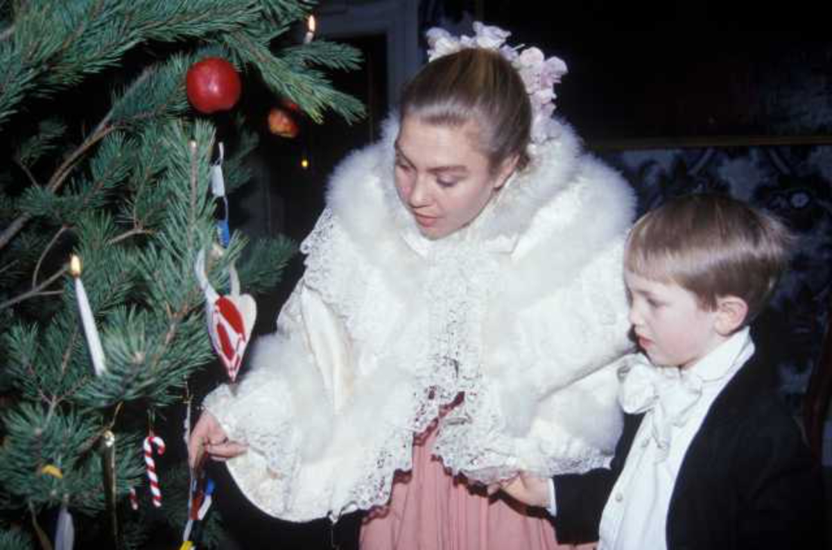 Det feires jul i Leikanger prestegård, bygning nummer 191 på Norsk Folkemuseum.Museumsansatt  samt et barn, begge i kostymer beundrer julepynten.