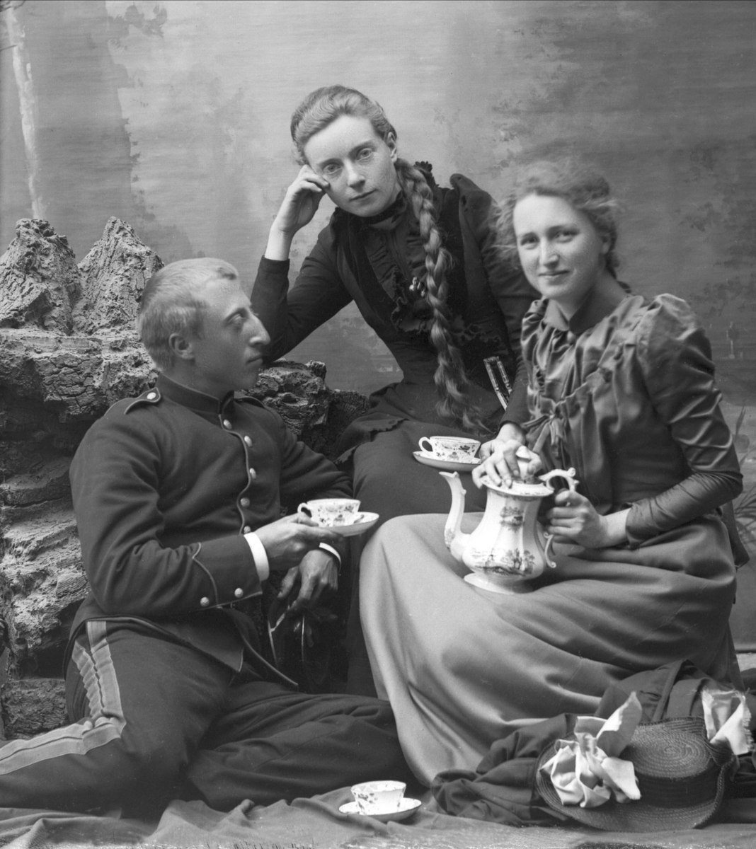 Gruppeportrett, mann i kadettuniform blir servert te av to unge kvinner.
