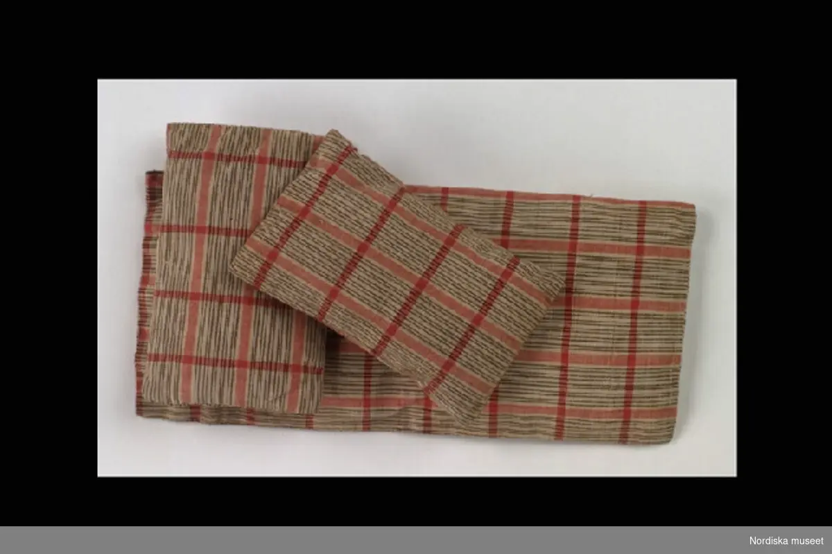 Inventering Sesam 1996-1999:
Sängkläder, docksängkläder, 3 delar.
a) Madrass av brun- och rödrandigt linne. L 23  B 11 cm.
b-c) 2 st kuddar av brun och rödrandigt linne. L 12  B  6,5  cm.
Birgitta Martinius 1997