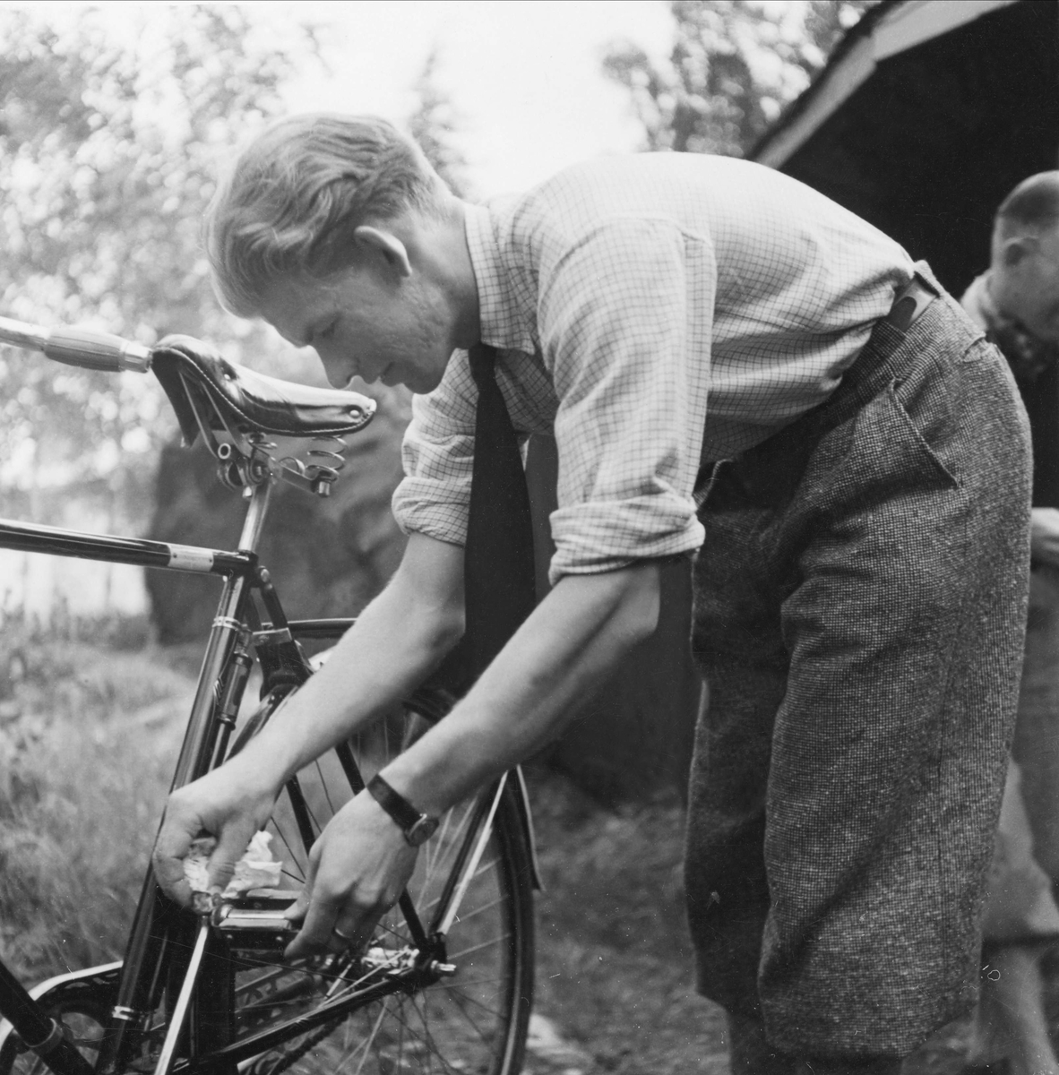 Cykelvård, en ung man klädd i knäbyxor och skjorta med uppkavlade ärmar, torkar tramporna på en cykel.