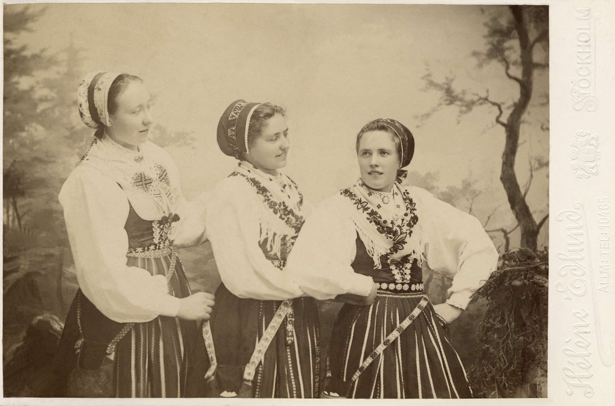 Tre unga kvinnor klädda i dräkter från Leksand, Dalarna.
