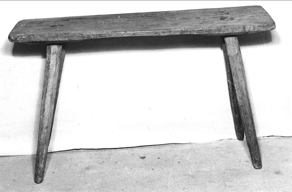Bänk, säte, av trä. Omålat. Under sitsen inristat: 1864 J. F.


