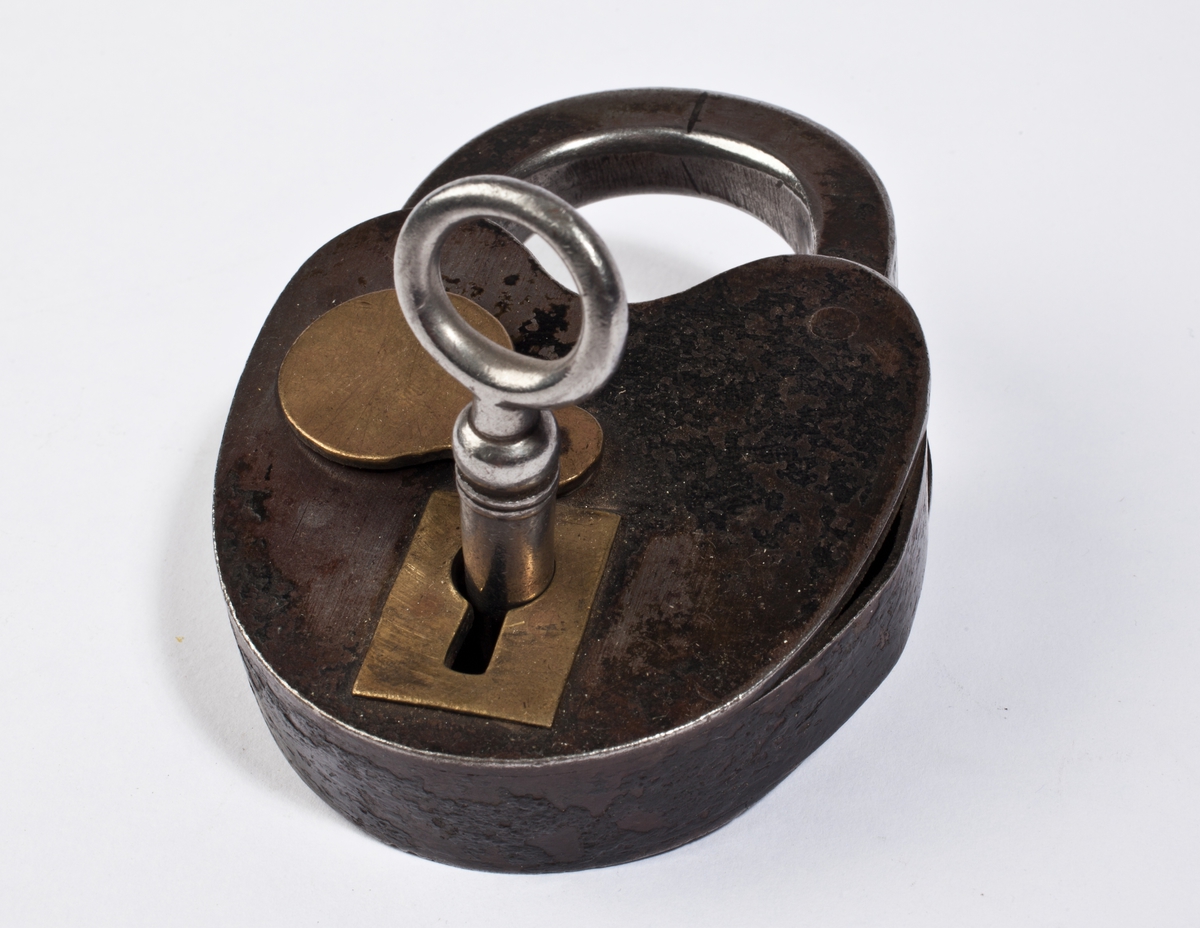 Hengelås med ovalt låsehus som er innsvingt øverst under bøylen. Låsen har tilhørende nøkkel og klaff til å dekke nøkkelhullet.