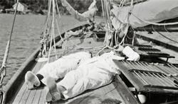 To personer hviler på dekk ombord i 12meter 'Raak' (b.1914).