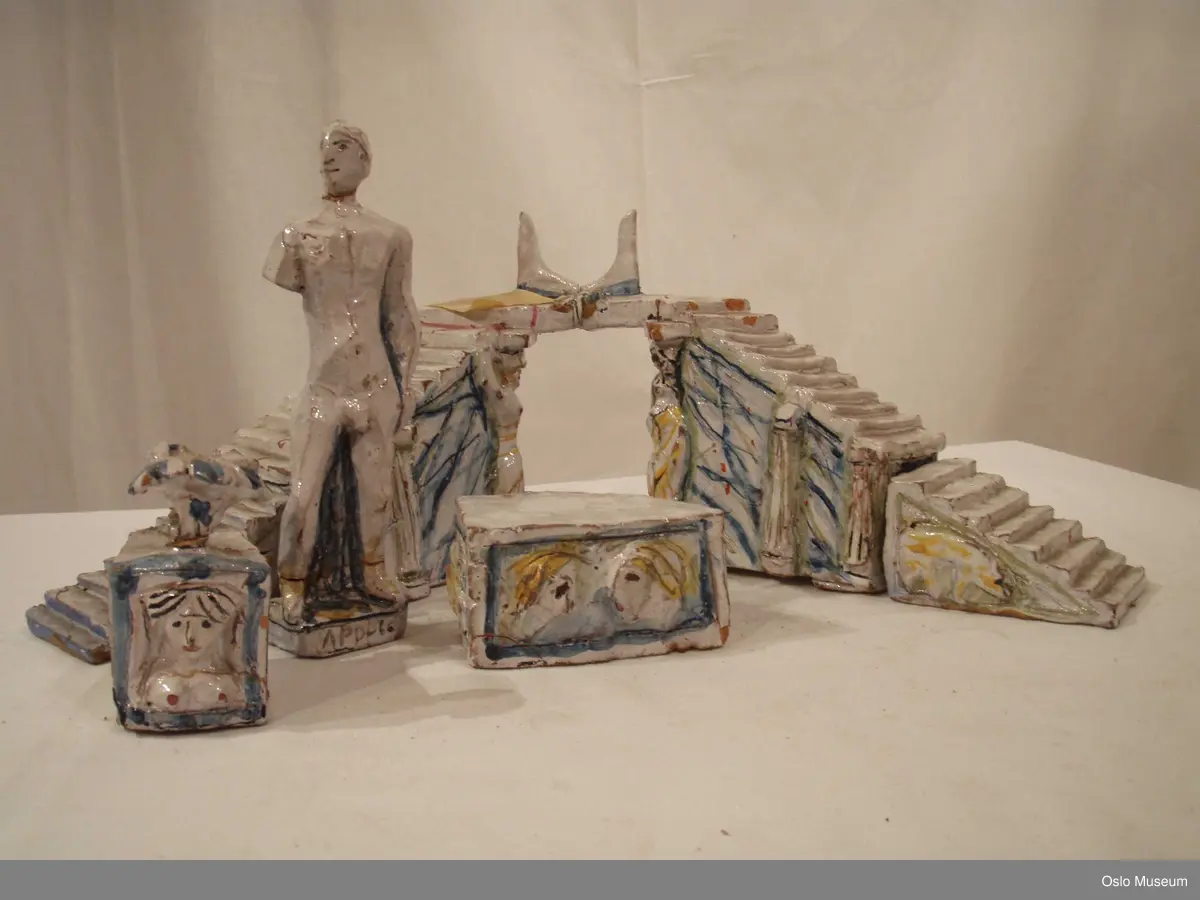 Scenografimodell av keramikk. Glasert i hvit bunnfarge med dekor/detaljer i blått og gult. 7 deler. Spesiallaget oppbevaringseske.