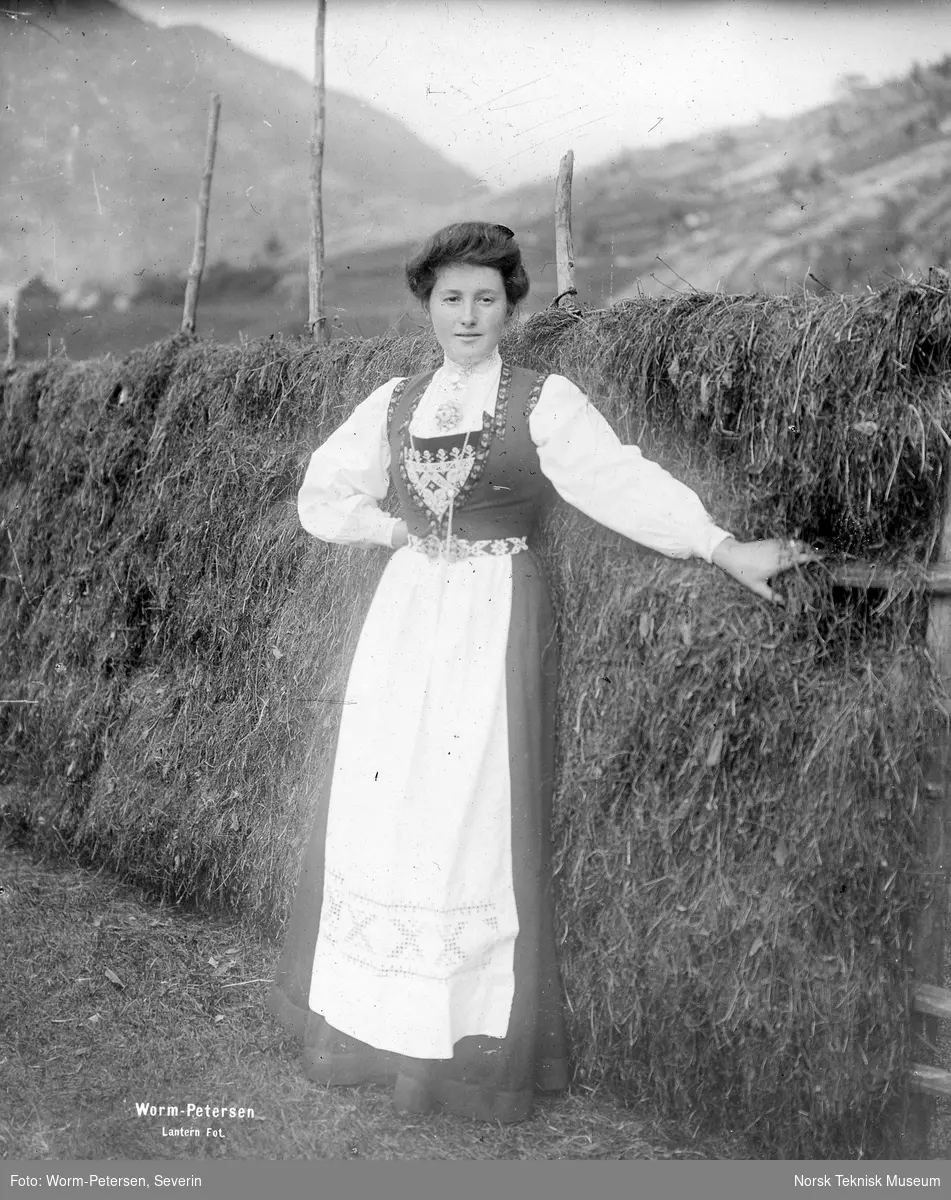 Kvinne i Hardangerbunad foran hesje, signert "Worm-Petersen Lantern Fot."