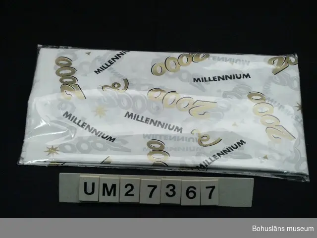 Bredd och höjd avser obruten förpackning.

Förpackning med vit bordsduk av plast med dekortexten "MiILLENNIUM 2000" i svart och guld. 
Oanvänd. Inköpt på Åhléns i Uddevalla för 29:50.

För information om Millennieinsamlingen, se UM27360.