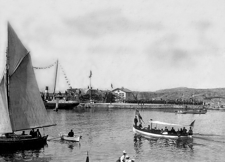 Medlemmar ur Coldino-orden placerar ett kors på kullen Malepert. 
Ett antal båtar syns i vattnet runt omkring. En större folksamlings står på kajen.