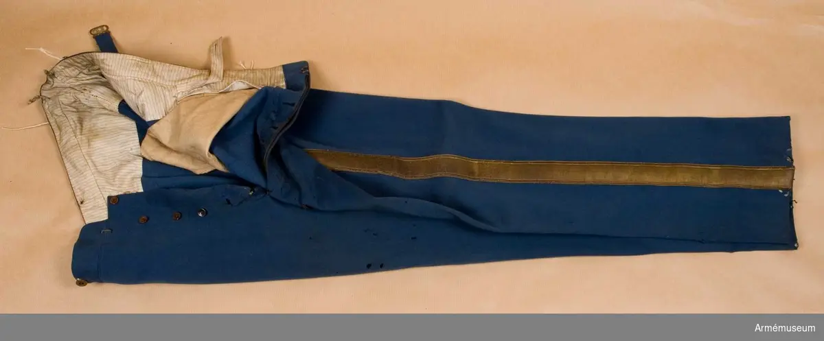 Grupp C I.
Byxor tillhörande uniform m/1868 med gradbeteckning m/1911 för general, Danmark.
Byxorna är tillverkade av ljusblått kläde, långa, försedda i yttre sömmen med 40 mm bred guldgalon och två fickor på sidan. På baksidan sitter spänntamp av kläde med spännen. Foder av vitt tyg med röda och blå ränder. Byxorna har knappar: sex stycken, små bruna av ben på sprundet och sex stycken av metall för hängslen.