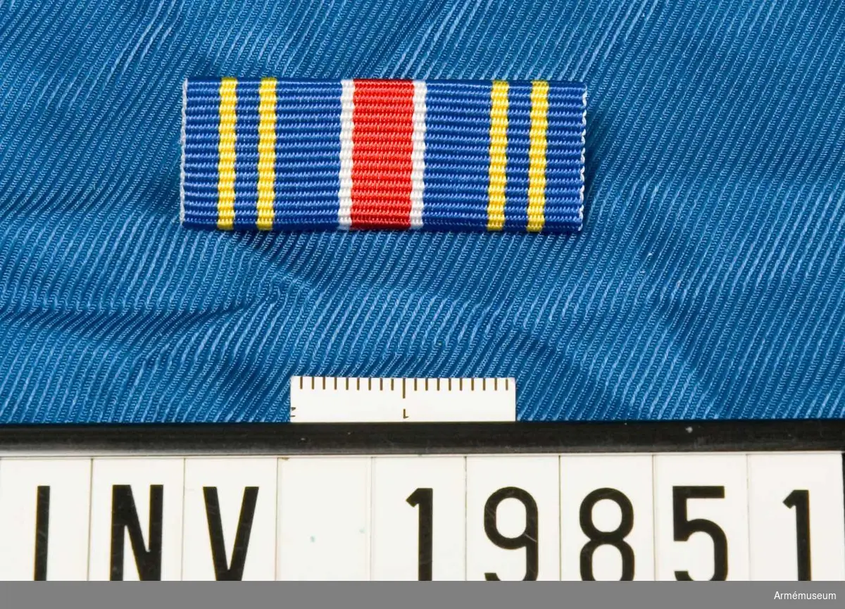 Släpspänne m/2000 Östra arméfördelningen 6. Bandet är blått med två smala gula ränder på varje sida. I mitten en bred röd rand åtfäljd på vardera sidan av ett vitt streck. Släpspännet förvaras i ett etui tillsammans med en medalj.