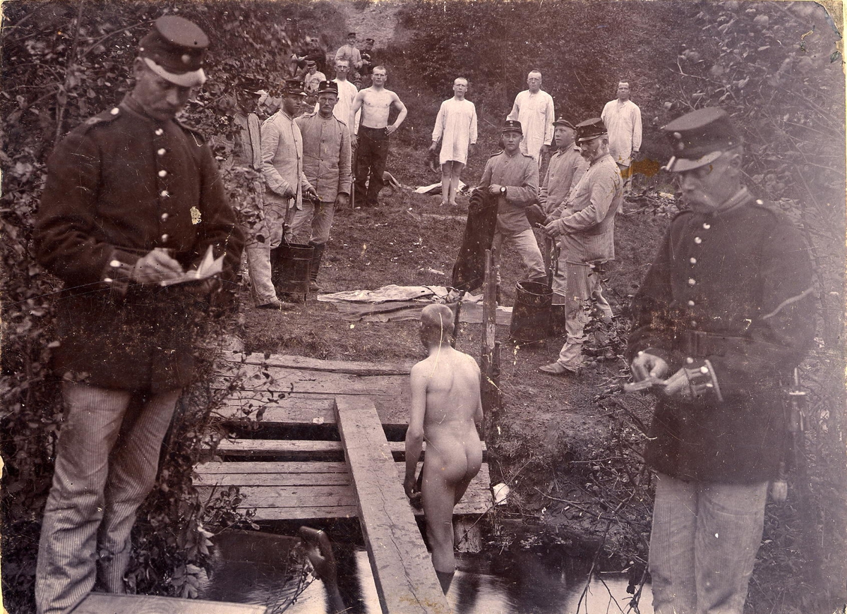Soldat ur Älvsborgs regemente I 15, badar i vattendrag vid Fristadhed. Flera soldater väntar på sin tur. I förgrunden två officerare som antecnar i bok.
