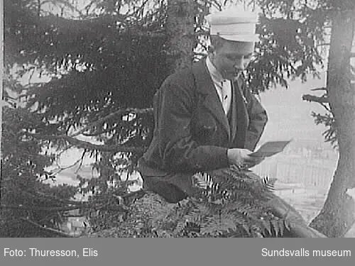 Gunnar Häggbom på en stubbe på Norra berget, läsandes ett brev. I bakgrunden skymtar Sundsvall.