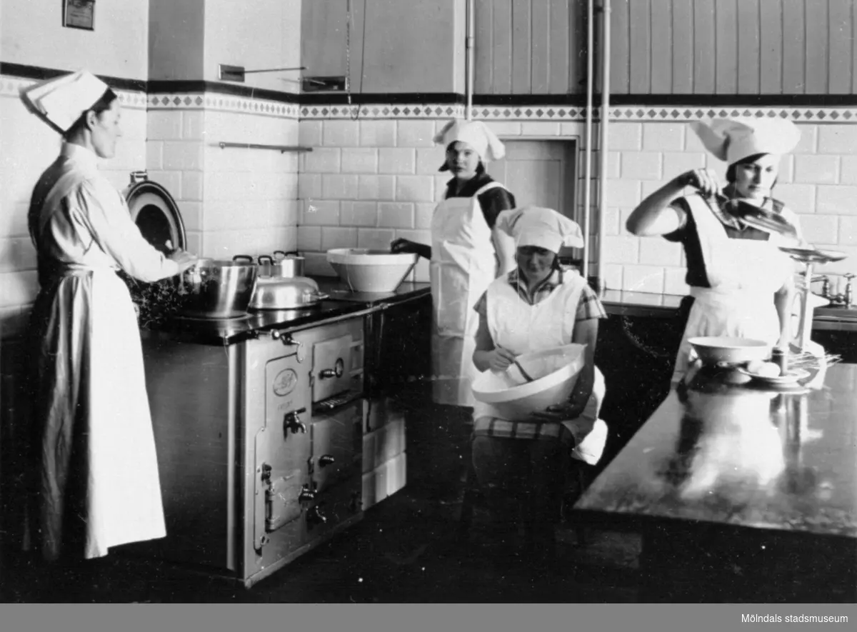 Skolköksinteriör på Trädgårdsskolan, 1900-tal. Fyra kvinnor lagar mat. Vedspis i köket. 
Se även MMF1992:0034