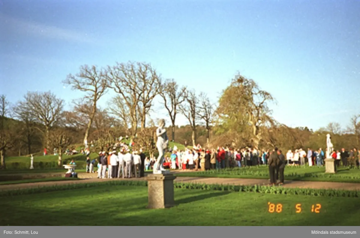 Människor som lyssnar till en studentkör i Gunnebo slottspark. I förgrunden ser man en skulptur ståendes på gräsmattan.