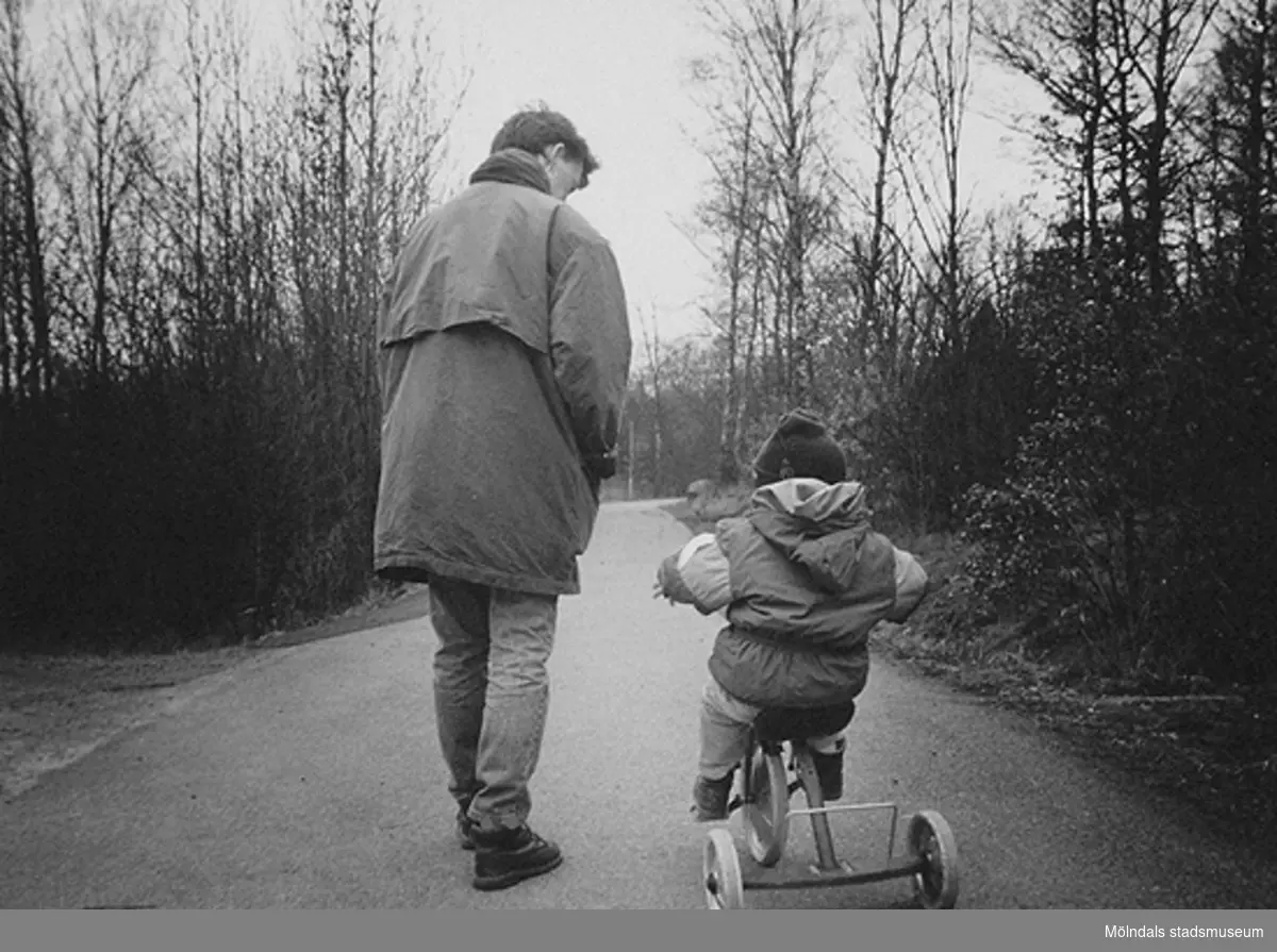 Ett litet barn som cyklar på en trehjuling och en kvinna går bredvid.
Bild som användes vid utställningen "Är du inte riktigt klok?" på Mölndals museum 1990.