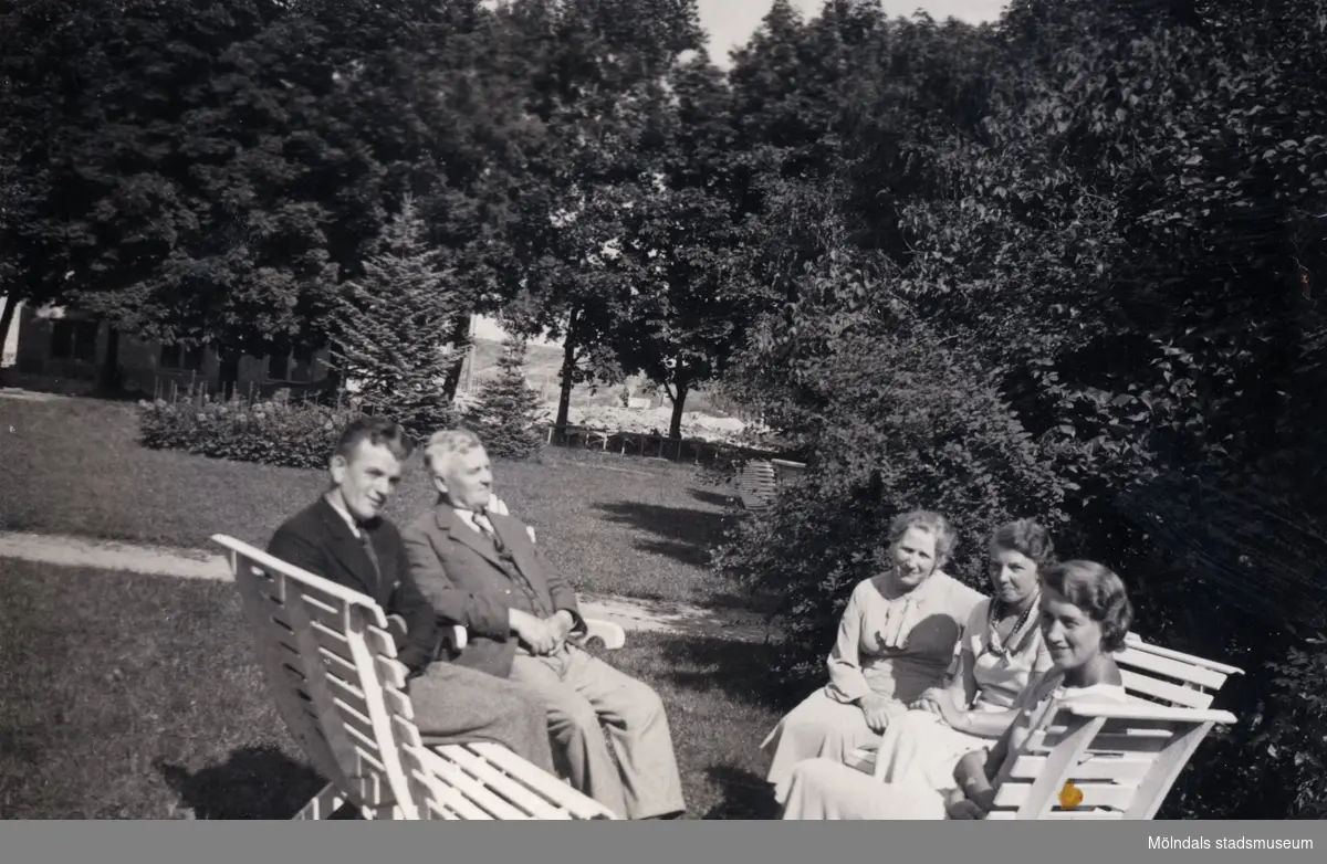 Kvinnor och män fotograferade sittandes i trädgården, Stretered i Kållered. Ivar Andersson sitter till vänster. "Ur Ivars fotoalbum."