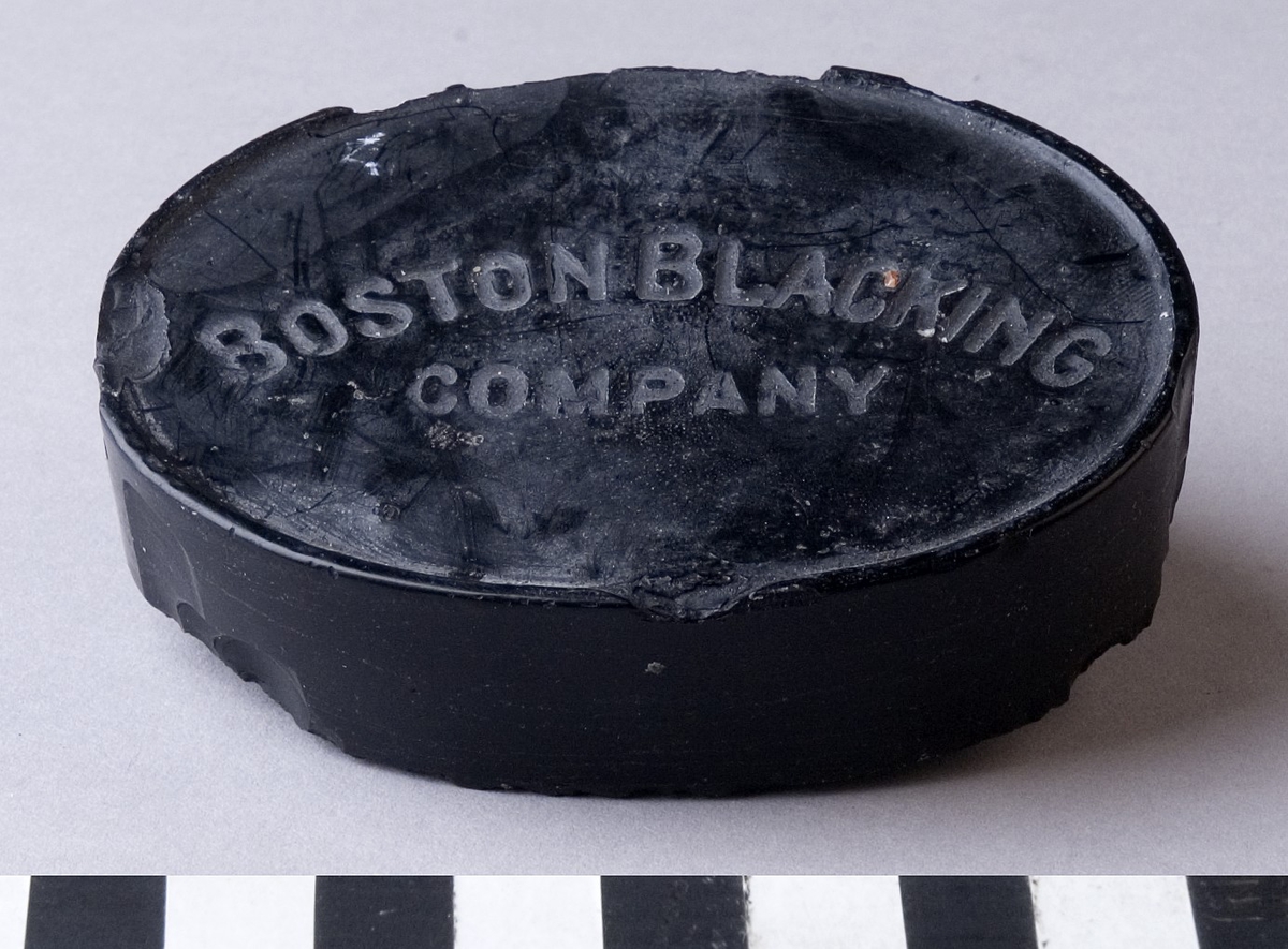 Färgvax, i form av en oval kaka i svart kulör av vax.
Märkt: "BOSTON BLACKING COMPANY".