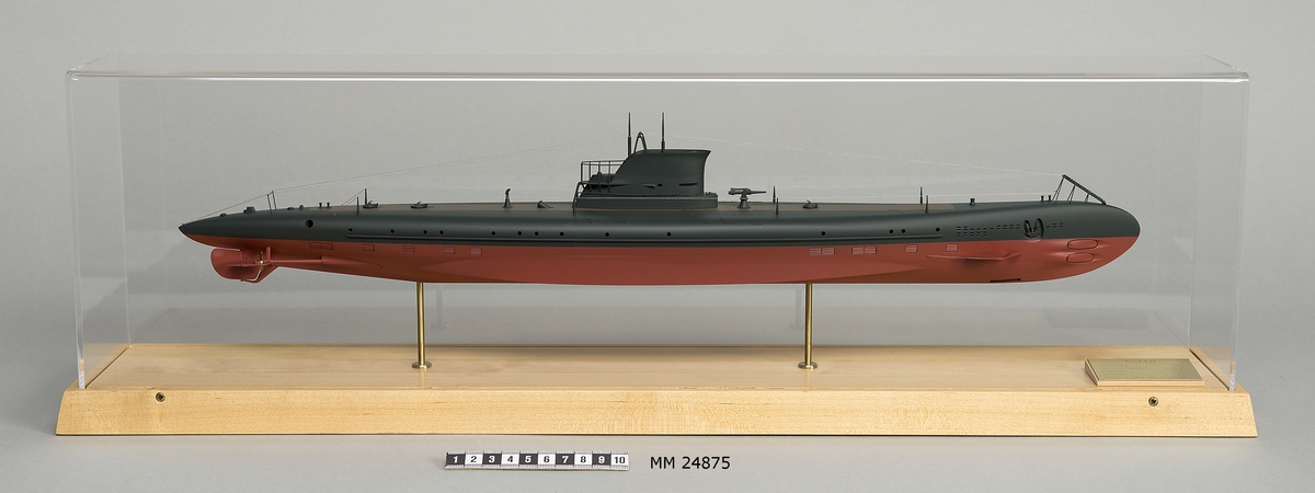 Ubåtsmodell Valen II i monter. Modell av alträ med detaljer av mässing, målad med cellulosafärg. Rött och svart skrov. Monter av plexiglas på träplatta. Mässingsbricka i montern med uppgifter om modellen.