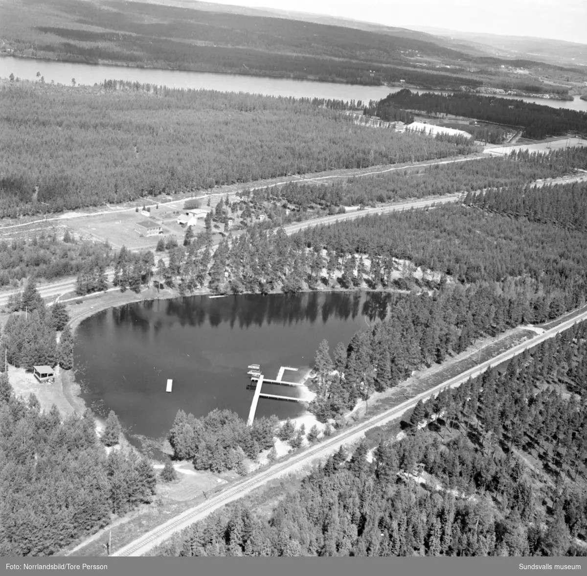 Flygfoton över Timrå med omnejd. Centrum, industriområdet, idrottsplatsen med "Grytan" och isladan, Östrandsfabriken, Vivstavarvstjärn, landsbygd.