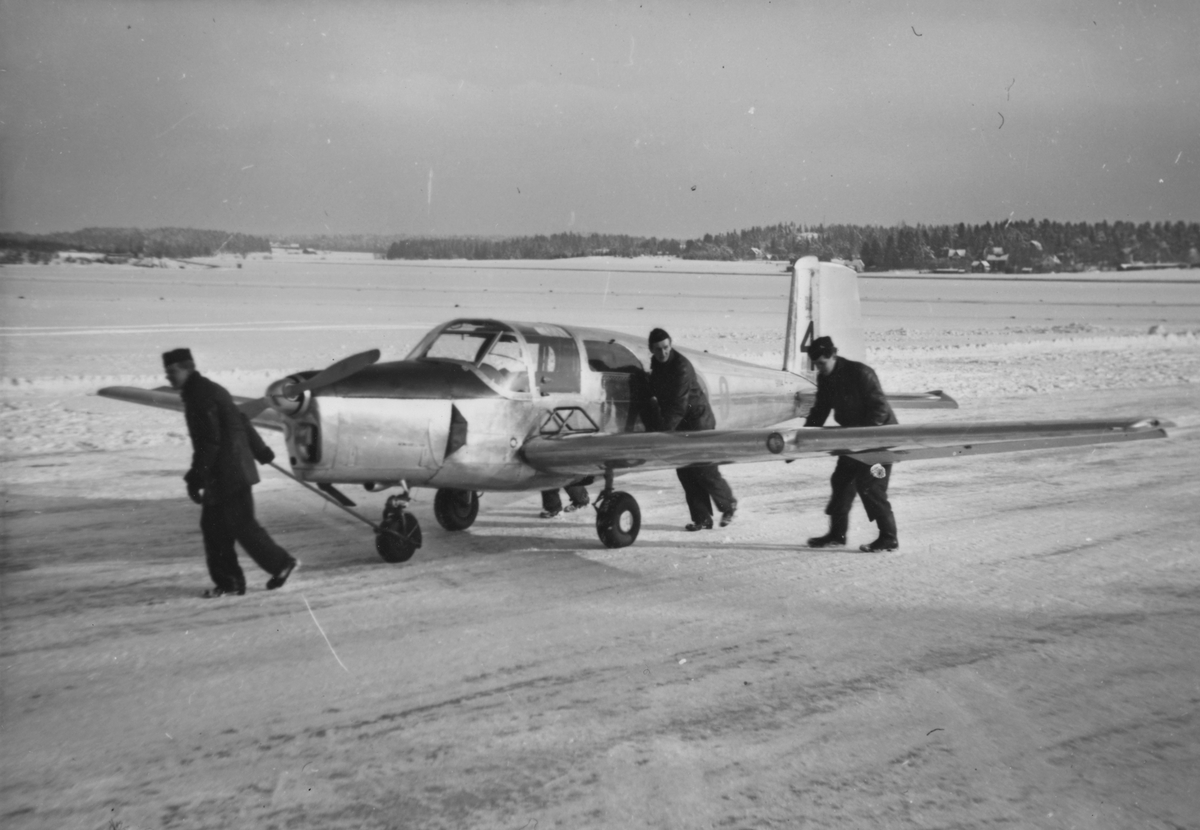 Flygplan TP 91 dras ut på flygfält på F 8 Barkarby, vintertid. Tre personer i arbete.