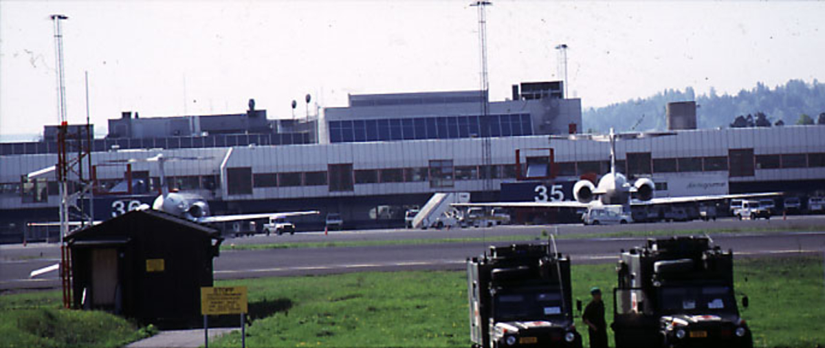 Lufthavn, i forgrunnen 2 kjøretøy fra Røde kors og 1 person i uniform. I bakgrunnen, 2 fly, flere kjøretøyer og terminalbygningen.