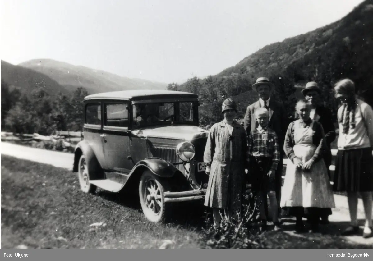 Den gamle kona med det kvite forkledet er Sigrid Venås, fødd 1870 i Nordre Venåsbakken (Venåsbakko,dialekt) Bilen er ein 1929 Nash Coach.
Biletet er teke i Venåskrysset.