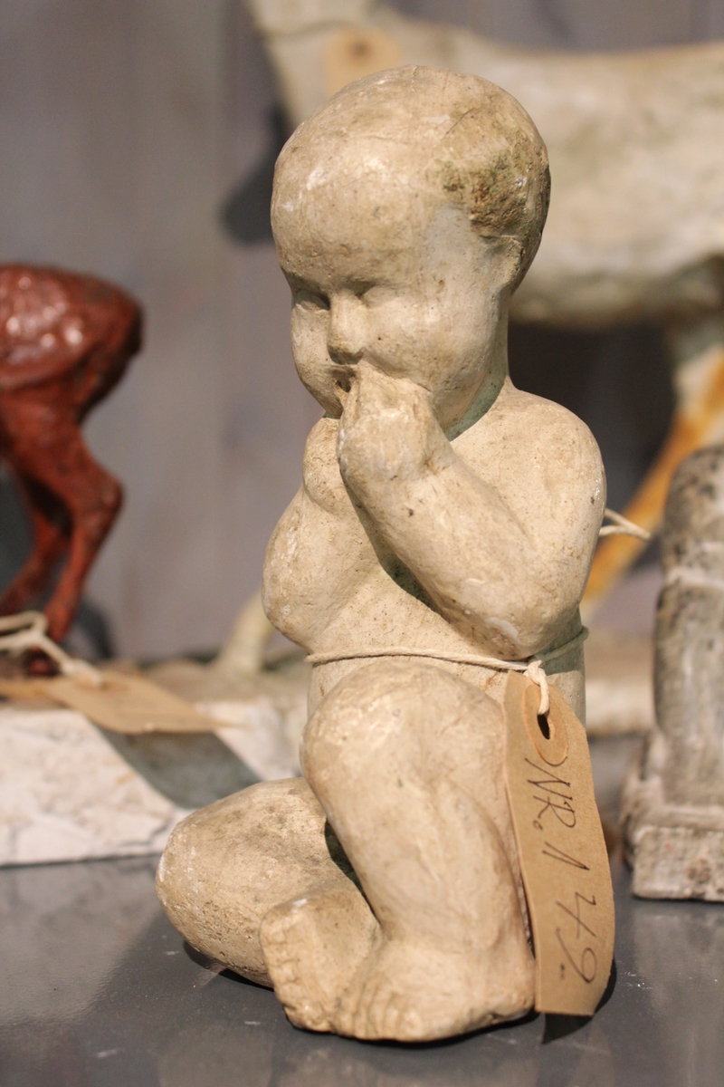 Skulptur av gips av et sittende barn som suger på fingrene