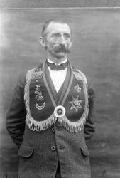 Studioportrett i halvfigur av mann med bart, briller, sløyfe