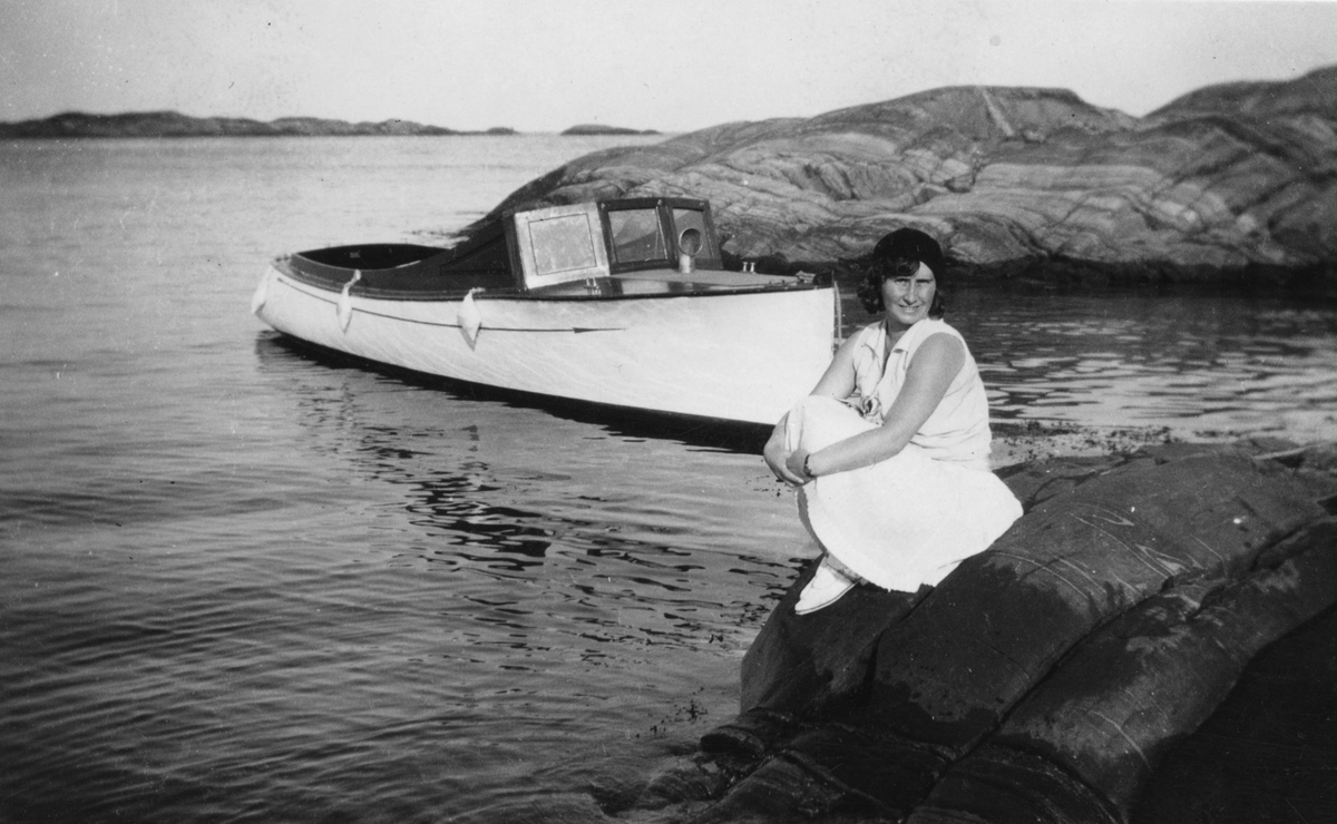 Marit sittende ved vannkanten med båten i bakgrunnen.