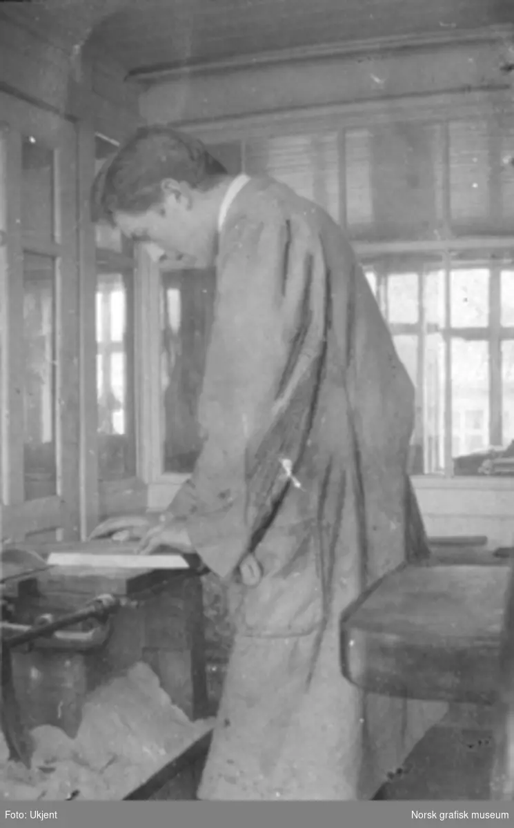 En ungmann står ved et arbeidsbord, antakelig en sag, innendørs på Dreyers Reproduksjonsanstalt i Stavanger. Tekst skrevet under bildet i albumet: "En sagfører (som har en daarlig sak)"