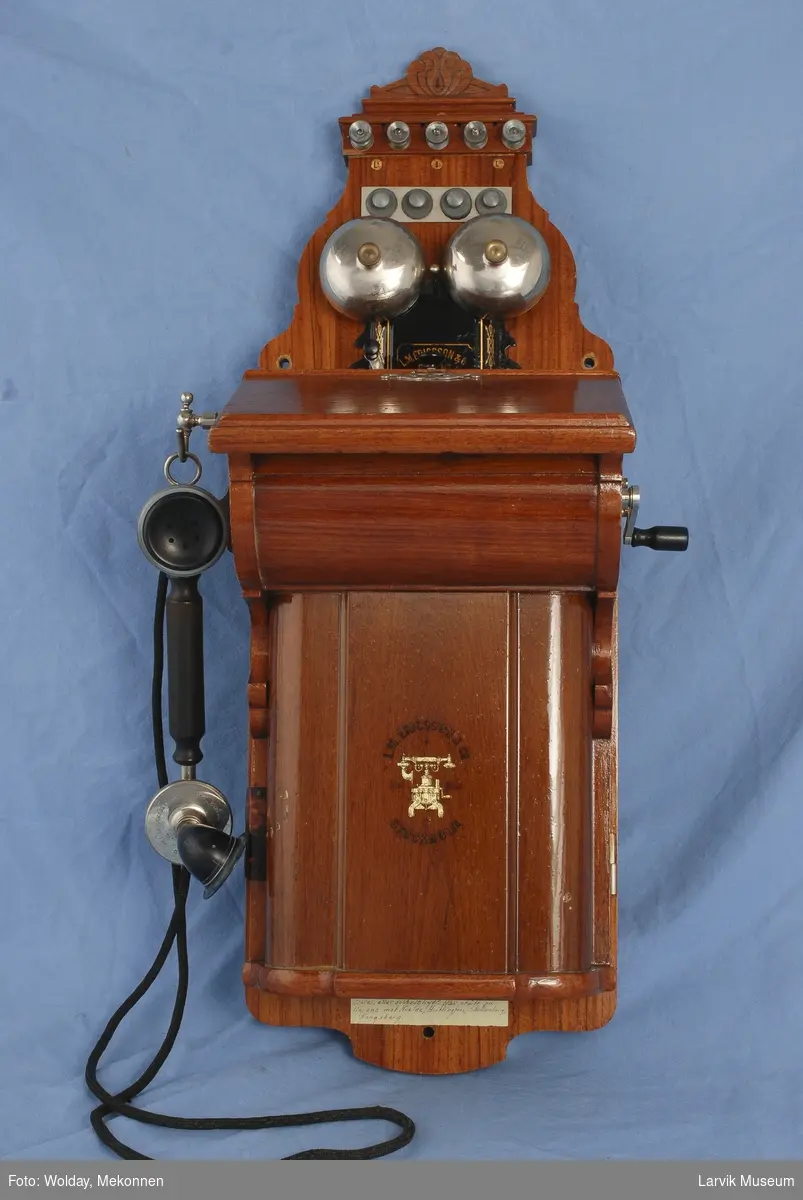 Form: Telefon kasse med lokk til å åpne. Telefon røret henger ved siden av. sveiv på andre siden.  
