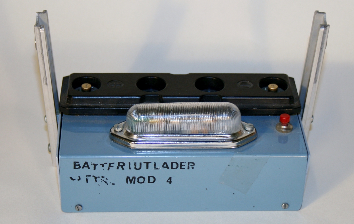 Rektangulær batteriutlader. Sokkel i gråblått metall. Sort støpsel på toppen der batteriet plasseres markert med + og -. Liten rød knapp og lampe.