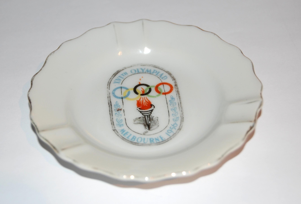 Hvitt rundt askebeger med logo for de olympiske sommerleker i Melbourne i 1956. I logoen er det motiv av en olympisk fakkel og de olympiske ringene.