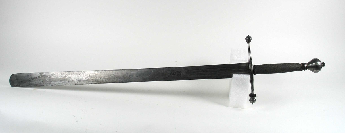 Skarprettersverd.  Pæreformet knapp med fasettetert dekor.
Tregrep viklet med rokkeskinn. 
Rette åttekantede parérstenger som ender i to dråper med kantet dekor. Rett tveegget klinge med ovalt tverrsnitt  og tre korte blodrender på hver side. Innslått tre smedstempler med kronede hoder.  På den ene siden er det gravert inn et hjul og på den andre siden en galge. Begge inngraveringer er innlagt med kobber.

