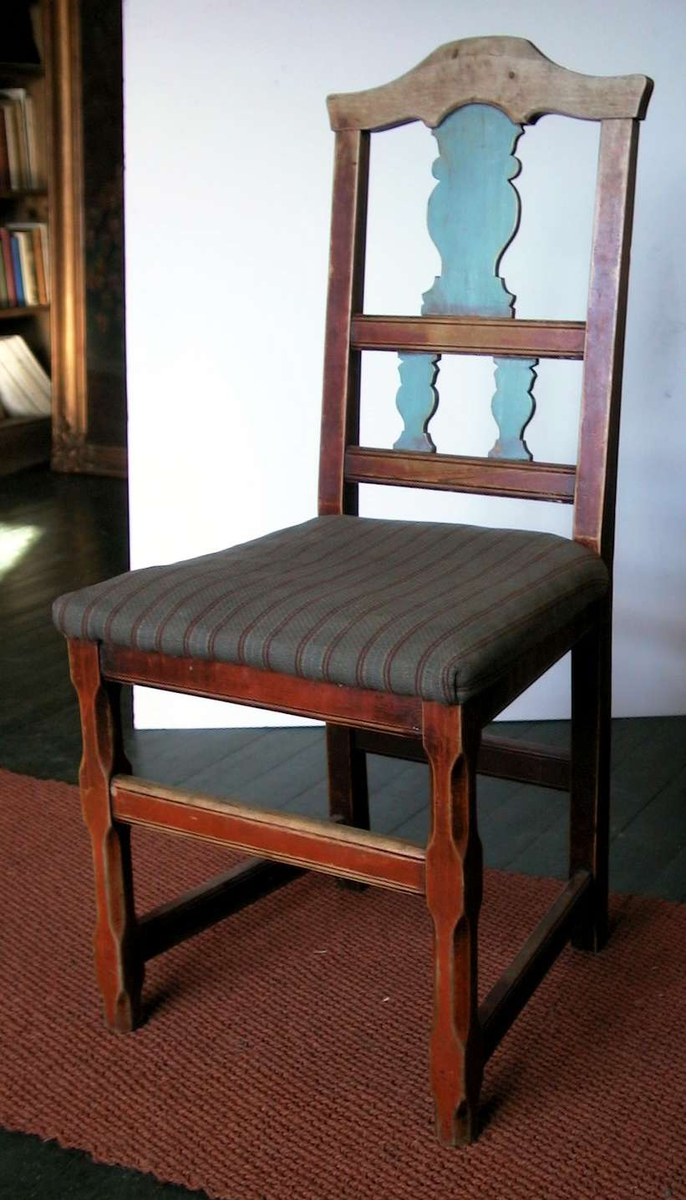 Spisestuestol med pute. Stolen er rød- og blåmalt. Malingen er nedslitt. Trekket er husflidsaktig og har brede grå striper med smale striper i bondeblått, rødt og gult.
