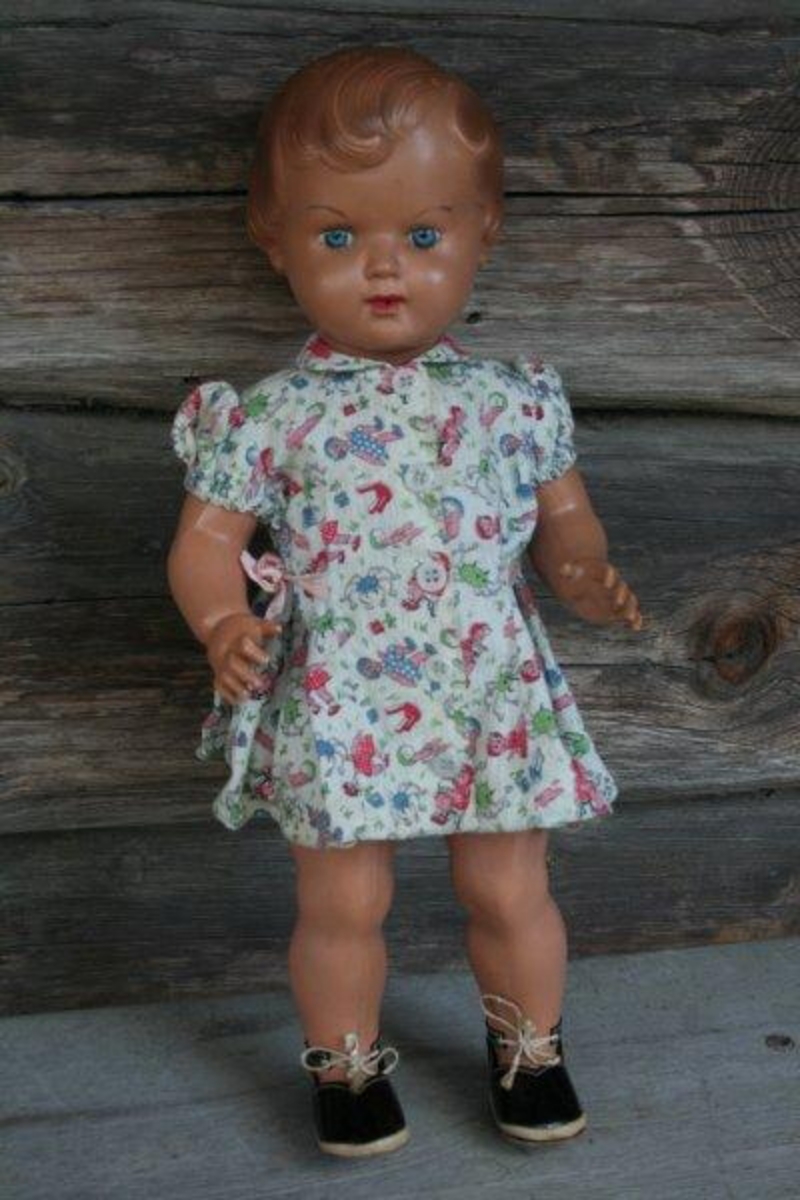 Hele dukken er støpt i celluloid. Påmalte blå øyne, brune øyenbryn, rød munn. Støpt, brunt hår. Kjolen er registrert som GH.07039.