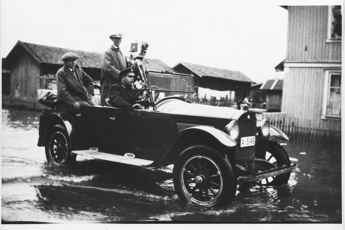 Filmfotograf i bil i arbeid under flommen i 1927.