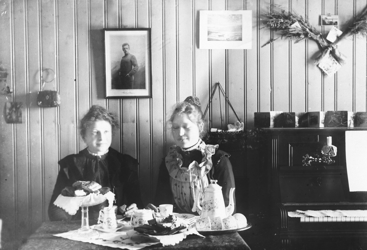 Interiør, stue med piano. To kvinner ved bordet med kaffe og kaker.