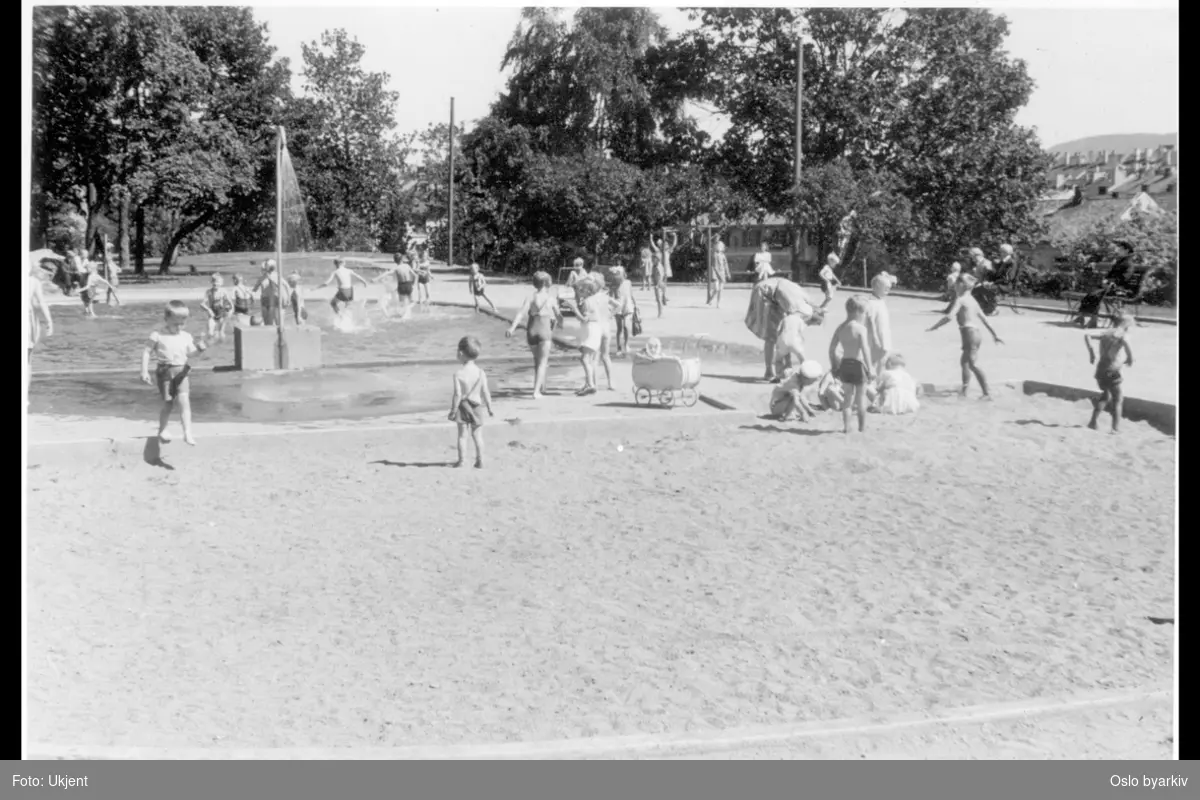 Lekende barn på øverste lekeplassen i parken. Vassebasseng / Plaskedam med dusj. Sandkasse. Barnevogn.