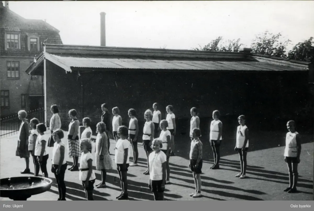 Pikeklasse i skolegården har gymnastikktime. (linjegymnastikk) Albumtittel: "Sofienberg skole femti år - første september 1933."
