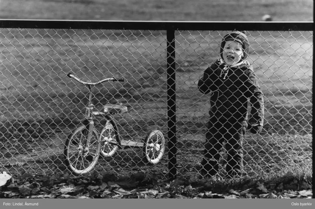 Gutt med trehjulssykkel bak gjerde. Fotografiet er fra prosjektet og boka ''Oslo-bilder. En fotografisk dokumentasjon av bo og leveforhold i 1981 - 82''. Kontakt Samfoto ved ev. bestilling av kopier.