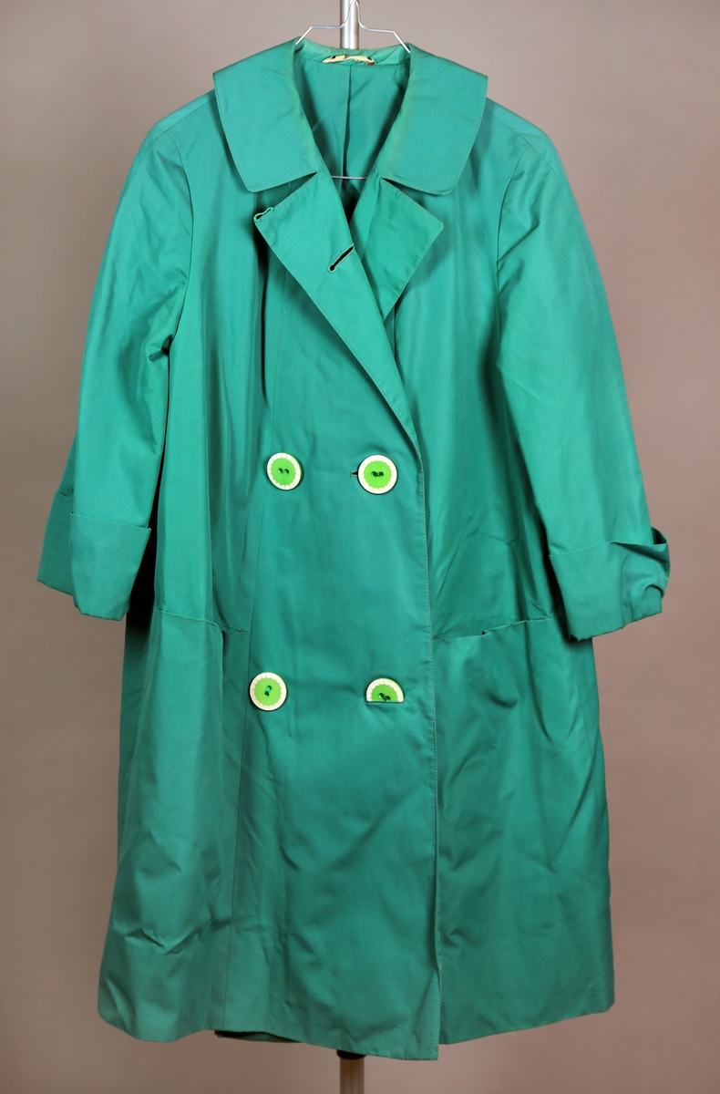 Lang frakk med dobbeltspent knepping, tilsammen 6 knapper i plast, som er store og grønne med en dekorativ kant. Det er lommer i front