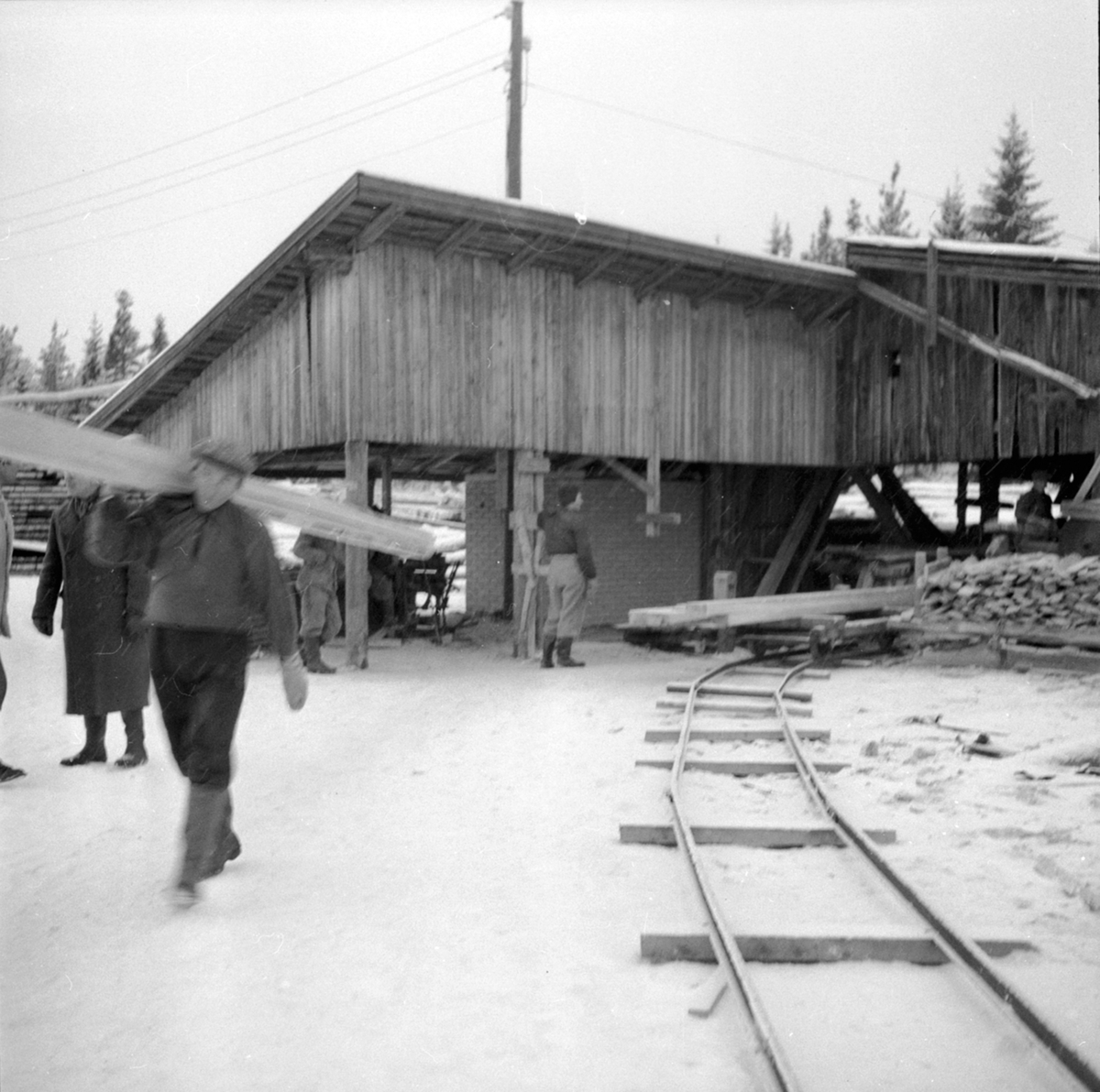 Sagbruk, mann bærer plank, skinnegang med vogner, Berger LAngmoen A/S, Brumunddal.