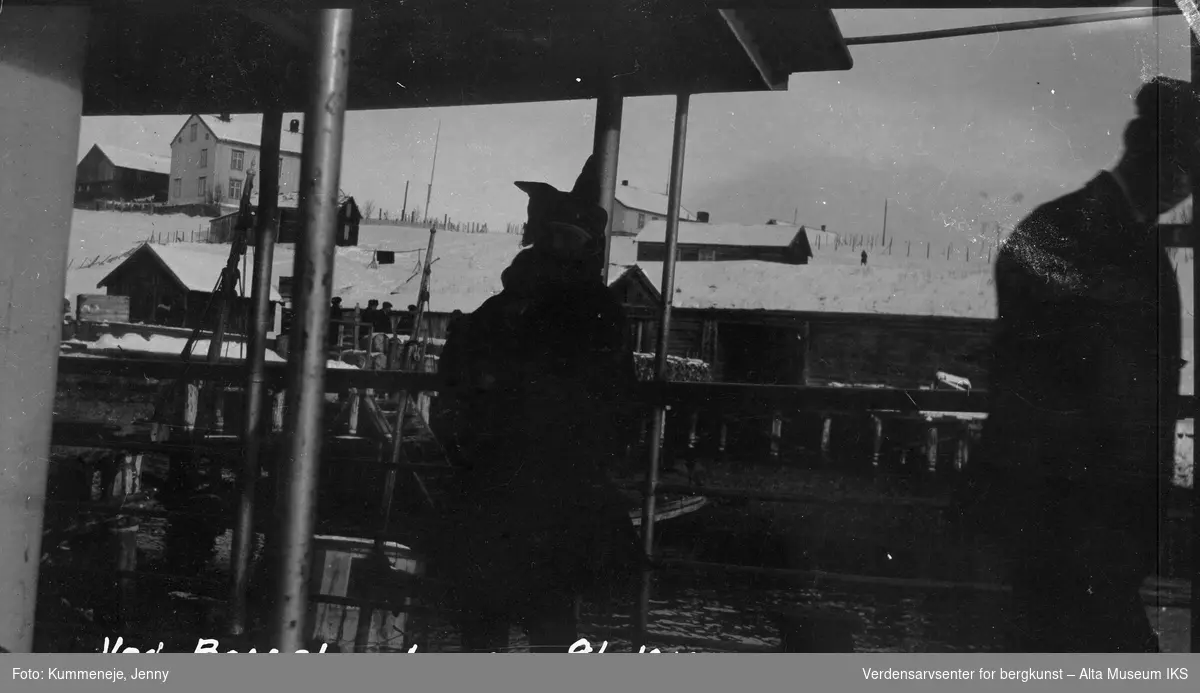 Mennesker i båt ved Bossekop brygge. Boliger i bakgrunn, 1919.