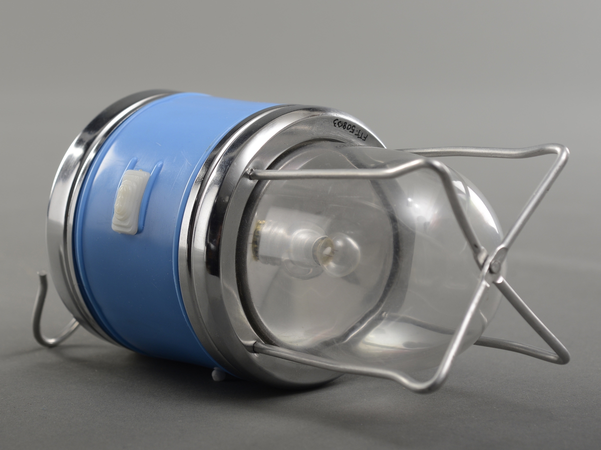 Batteridrevet lanterne med krok i ene enden og liten glødepære beskyttet av en glasskuppel i andre enden. Glasskuppelen er beskyttet av stålstenger i kryss. Lykta er hovedsaklig matt blå, med render av metal, med en skyveknapp i hvit plast.